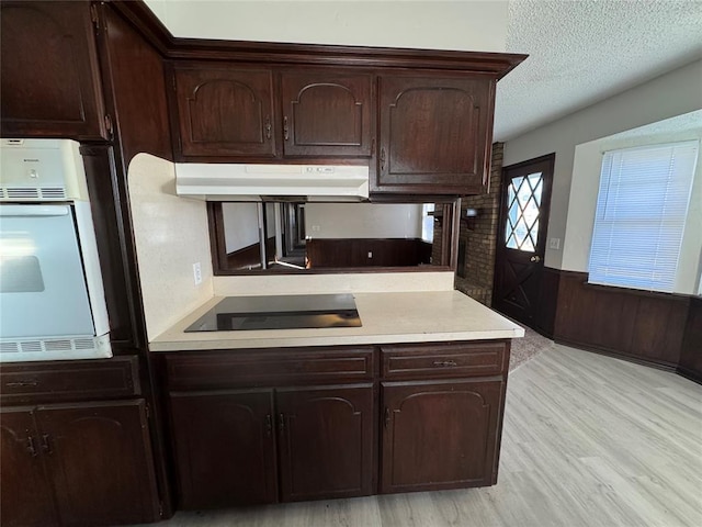 kitchen featuring dark brown cabinets, a textured ceiling, white oven, black electric cooktop, and wooden walls