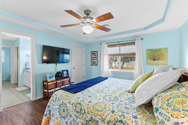 bedroom featuring hardwood / wood-style floors, ensuite bathroom, ceiling fan, and a tray ceiling