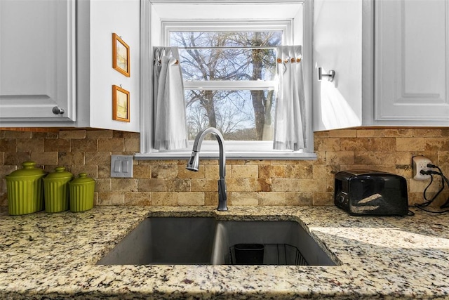 kitchen featuring white cabinets, decorative backsplash, light stone countertops, and sink