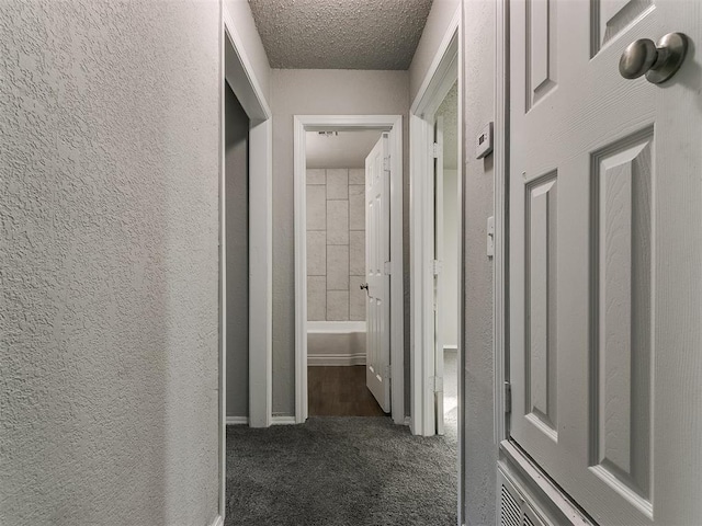 hall featuring a textured ceiling and dark carpet