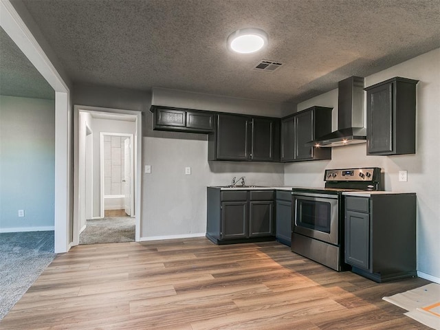 kitchen with a textured ceiling, stainless steel range with electric cooktop, wall chimney range hood, and light wood-type flooring