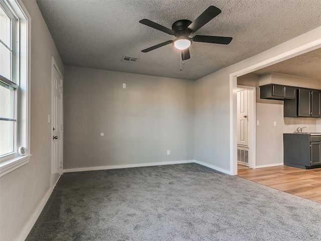 unfurnished living room featuring ceiling fan, light colored carpet, and a textured ceiling