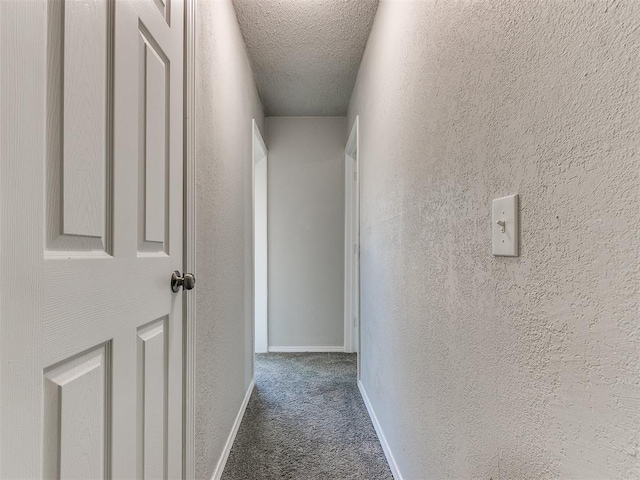 hallway featuring dark colored carpet and a textured ceiling