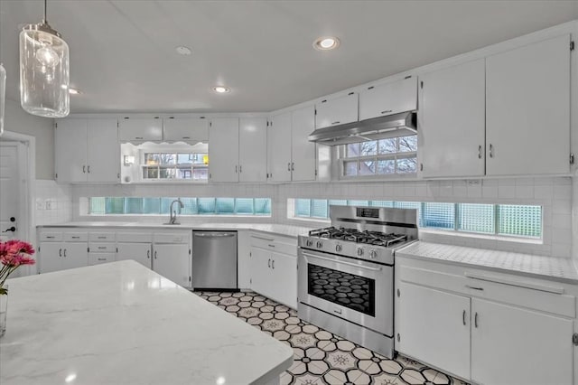 kitchen with stainless steel appliances, decorative backsplash, white cabinetry, and hanging light fixtures