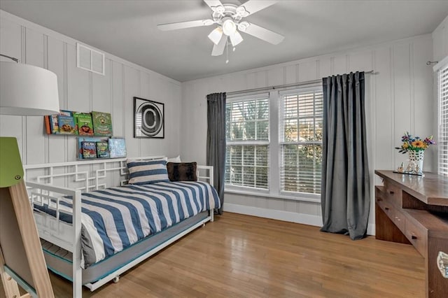 bedroom with ceiling fan, baseboards, light wood-style flooring, and a decorative wall