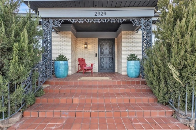 view of exterior entry featuring a porch and brick siding