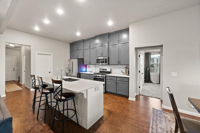 kitchen with sink, stainless steel appliances, a kitchen breakfast bar, an island with sink, and gray cabinets