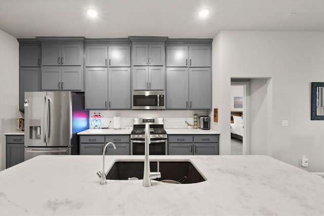 kitchen featuring gray cabinetry, light stone counters, and appliances with stainless steel finishes