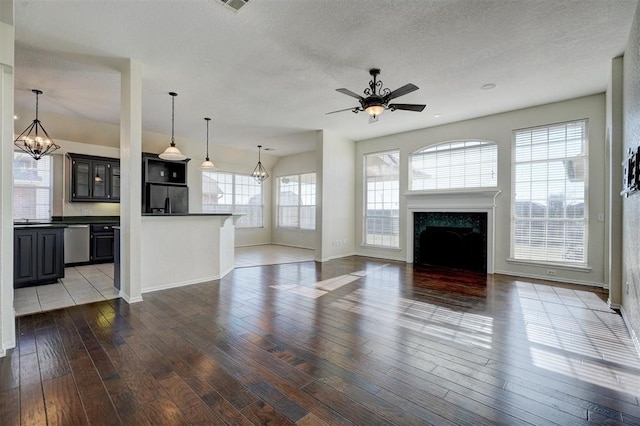 unfurnished living room with a fireplace, a healthy amount of sunlight, ceiling fan with notable chandelier, and dark wood-type flooring