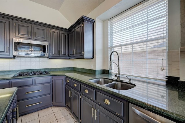 kitchen with sink, stainless steel appliances, dark stone countertops, lofted ceiling, and light tile patterned floors