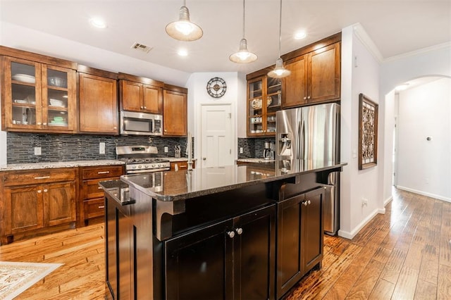 kitchen featuring appliances with stainless steel finishes, backsplash, crown molding, dark stone countertops, and a center island