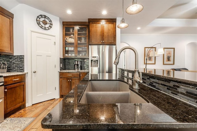 kitchen featuring pendant lighting, dark stone counters, sink, light hardwood / wood-style flooring, and stainless steel fridge