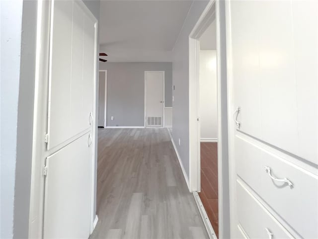 corridor featuring light wood finished floors, baseboards, and visible vents