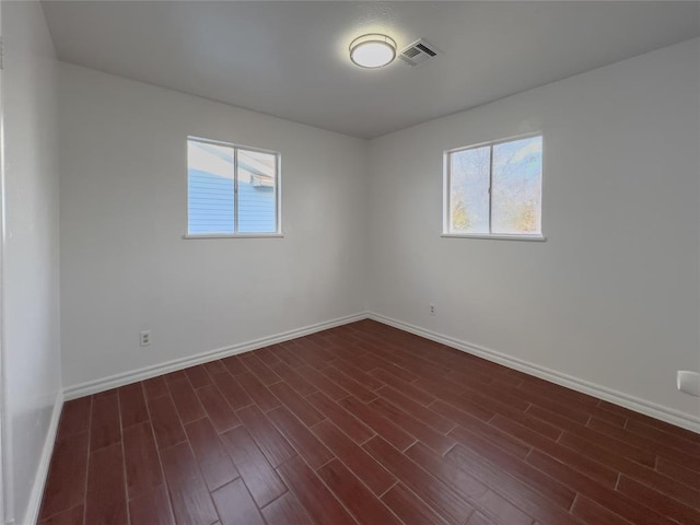 unfurnished room with a wealth of natural light, baseboards, visible vents, and dark wood-type flooring