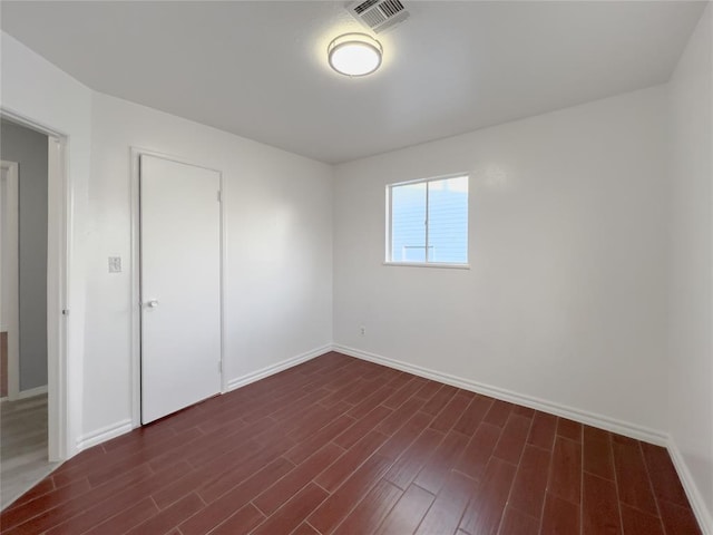 unfurnished room featuring dark wood-style floors, visible vents, and baseboards