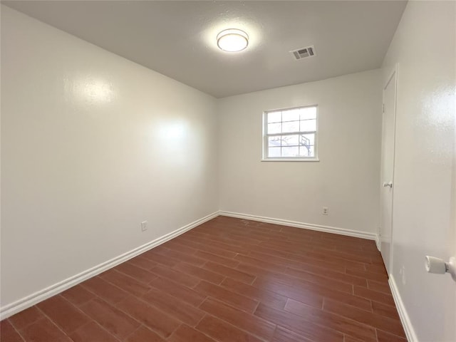 unfurnished room featuring dark wood-type flooring, visible vents, and baseboards