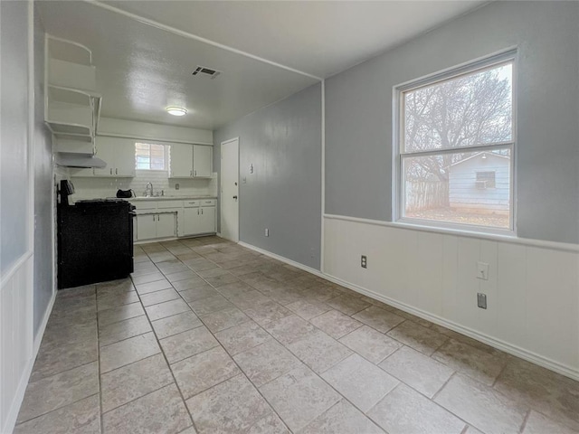 kitchen with visible vents, black stove, a wainscoted wall, light countertops, and white cabinetry