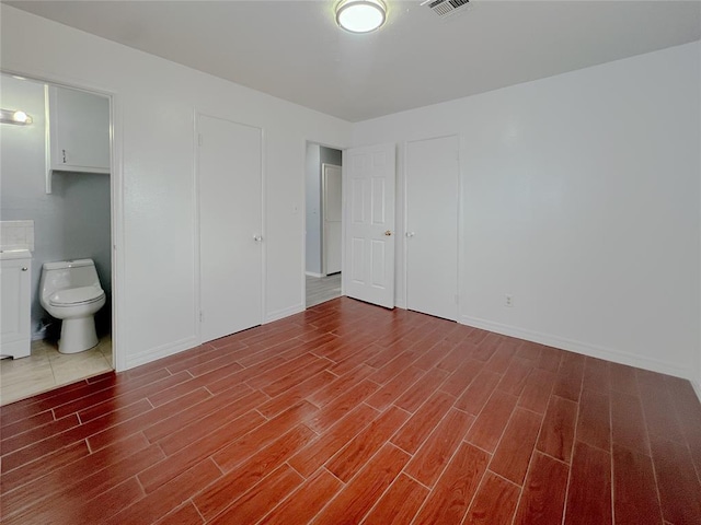 unfurnished bedroom with baseboards, ensuite bathroom, and wood finished floors