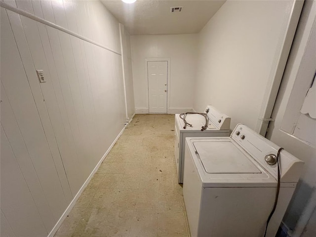 clothes washing area with light floors, wood walls, washing machine and clothes dryer, and visible vents