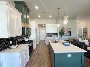 kitchen with stove, white cabinetry, hanging light fixtures, and an island with sink