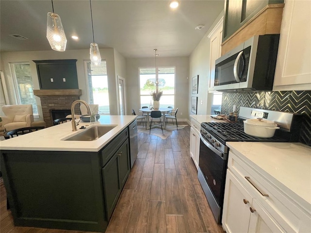 kitchen featuring white cabinetry, sink, hanging light fixtures, stainless steel appliances, and a kitchen island with sink