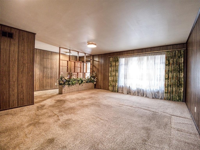 carpeted empty room featuring wood walls