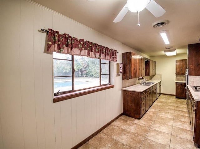 kitchen with sink, ceiling fan, wooden walls, and dark brown cabinetry