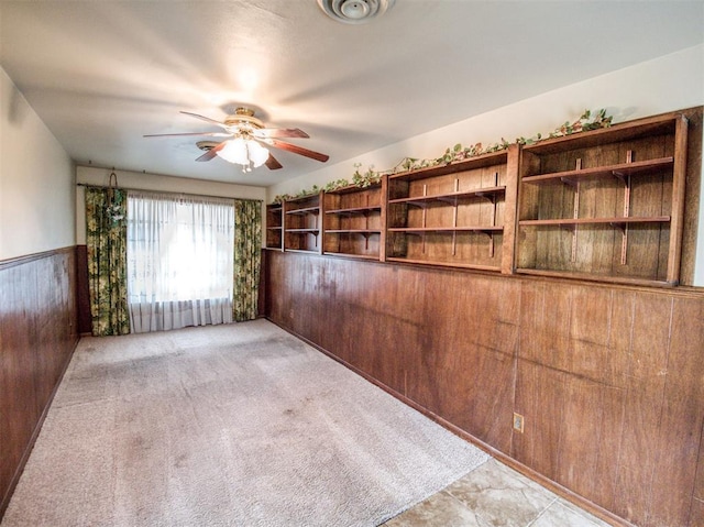 empty room with light colored carpet, ceiling fan, and wooden walls