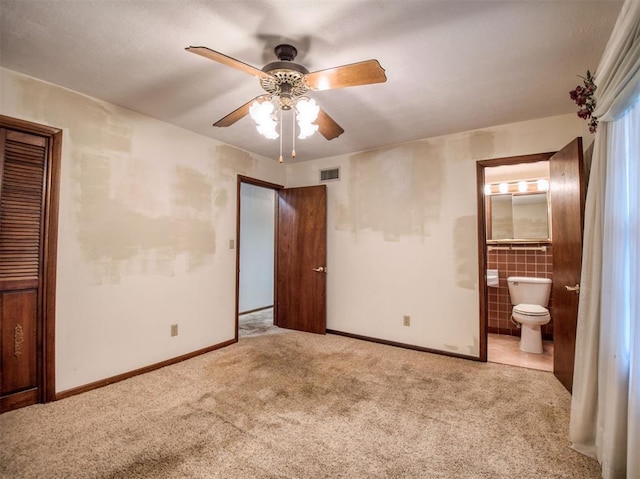 unfurnished bedroom featuring connected bathroom, a closet, light carpet, ceiling fan, and tile walls