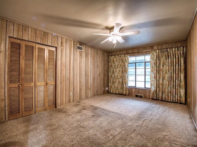 unfurnished bedroom featuring ceiling fan, wood walls, and carpet flooring