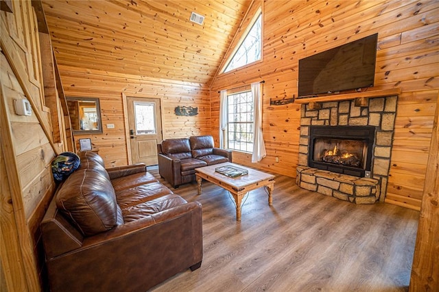 living room with wood walls, wooden ceiling, high vaulted ceiling, a stone fireplace, and hardwood / wood-style flooring