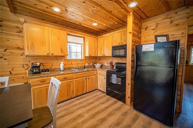 kitchen featuring dark stone countertops, sink, wood walls, and black appliances