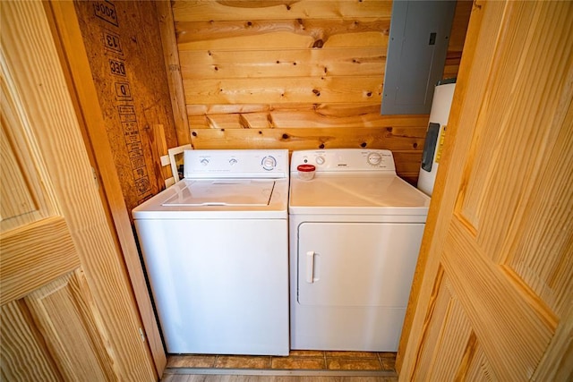 clothes washing area with electric panel, wood walls, and washing machine and clothes dryer