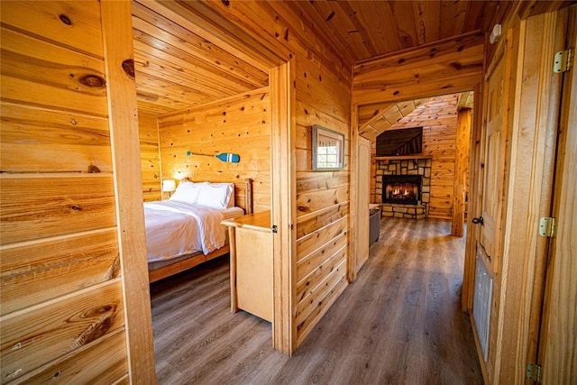 unfurnished bedroom featuring dark hardwood / wood-style flooring, a stone fireplace, wooden ceiling, and wood walls