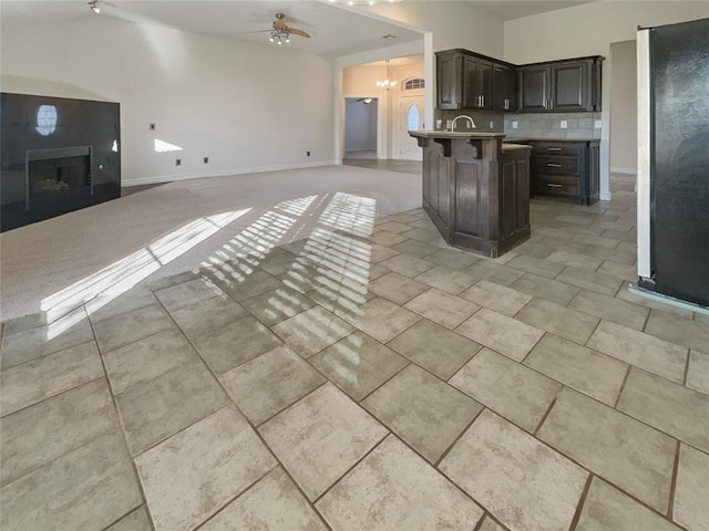 kitchen featuring a kitchen island with sink, ceiling fan with notable chandelier, tasteful backsplash, a kitchen bar, and dark brown cabinetry