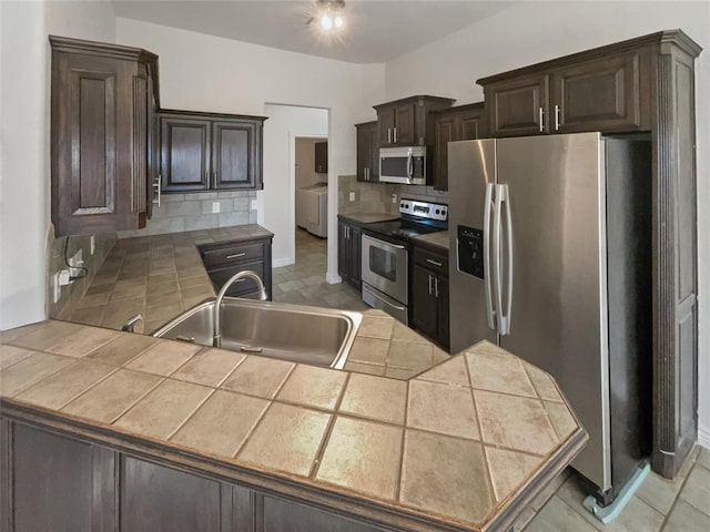 kitchen with tile countertops, sink, dark brown cabinets, stainless steel appliances, and washer / clothes dryer