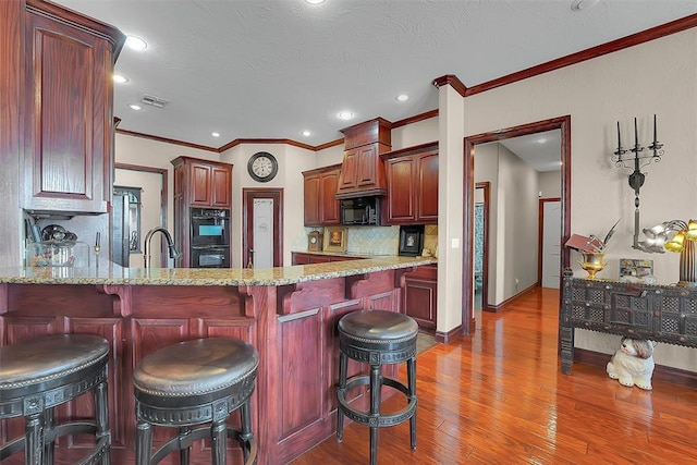 kitchen with a breakfast bar, tasteful backsplash, kitchen peninsula, light stone countertops, and black appliances