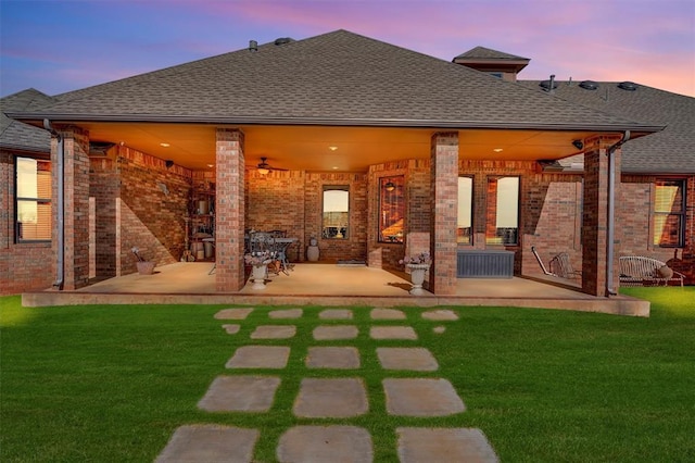 back house at dusk featuring a yard, a patio, and ceiling fan