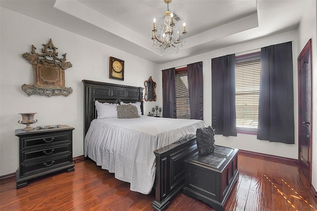 bedroom with a raised ceiling, dark hardwood / wood-style floors, and an inviting chandelier