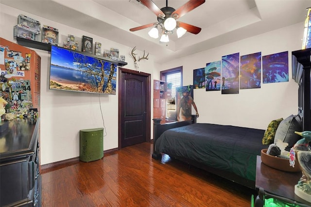 bedroom with ceiling fan, a tray ceiling, and hardwood / wood-style floors