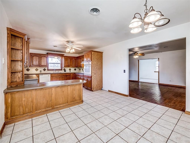 kitchen with kitchen peninsula, decorative backsplash, white appliances, ceiling fan with notable chandelier, and light tile patterned floors