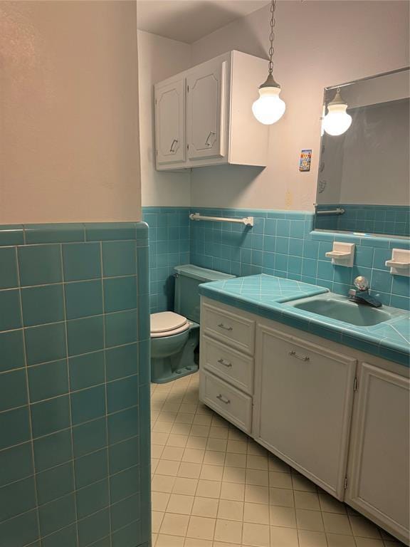 bathroom with toilet, vanity, tile patterned floors, and tile walls