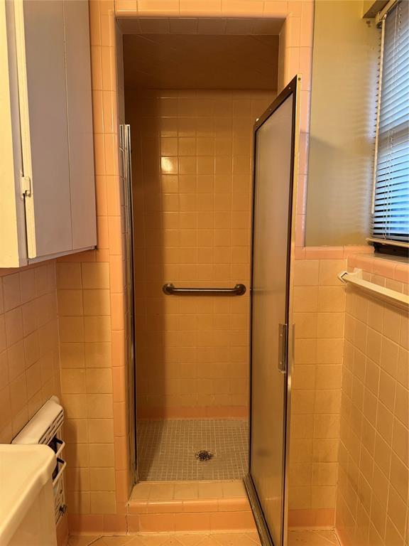 bathroom with an enclosed shower, toilet, and tile walls