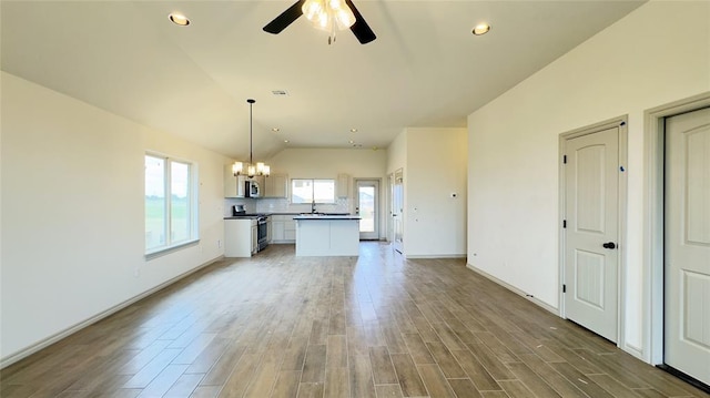 unfurnished living room featuring a wealth of natural light, ceiling fan with notable chandelier, vaulted ceiling, and hardwood / wood-style flooring