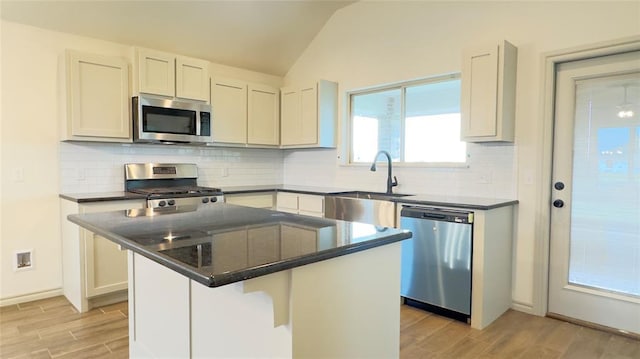 kitchen featuring appliances with stainless steel finishes, backsplash, a breakfast bar, vaulted ceiling, and a center island