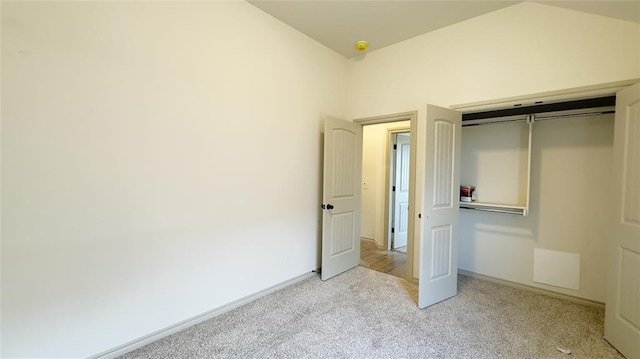 unfurnished bedroom with light colored carpet, a closet, and lofted ceiling