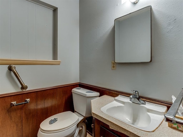 bathroom featuring vanity, toilet, and wooden walls