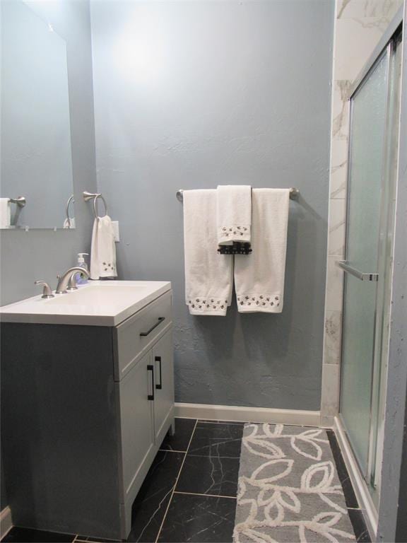 full bath with baseboards, vanity, marble finish floor, and a shower stall