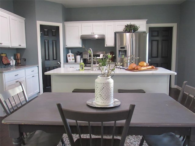 kitchen with a kitchen bar, stainless steel fridge, white cabinets, and a center island with sink