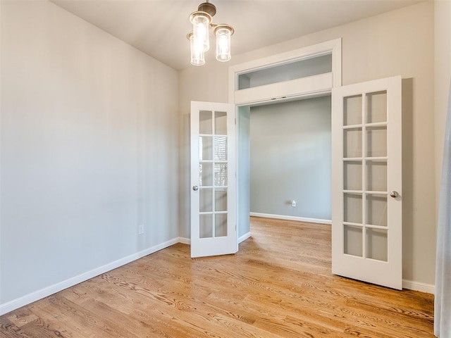 unfurnished room featuring a chandelier, light wood-type flooring, and french doors